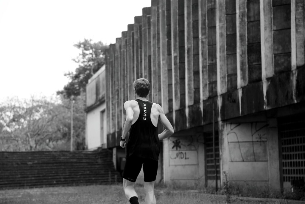 Corredor de costas correndo ao lado de prédio brutalista, usando roupas esportivas da Hound